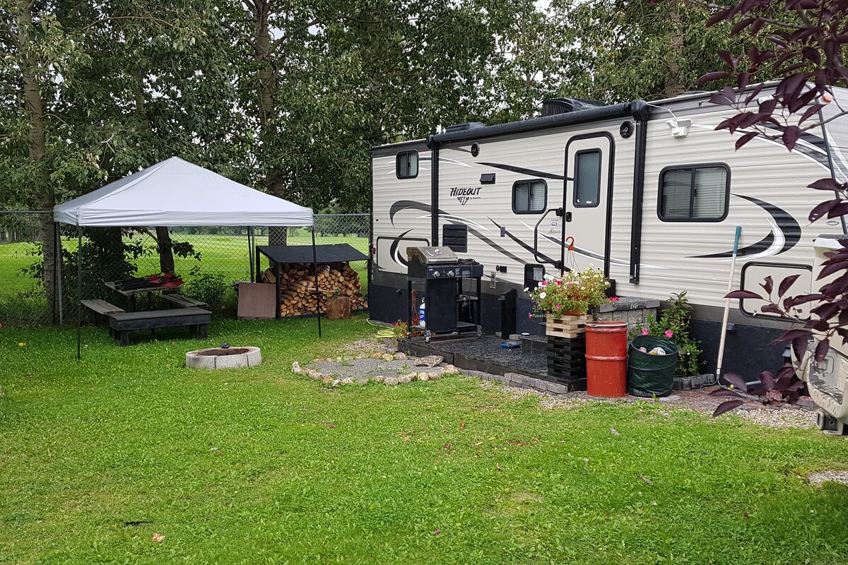 Cozy back-in campsite with canopy, picnic table, fire pit, stacked firewood, and golf course in background